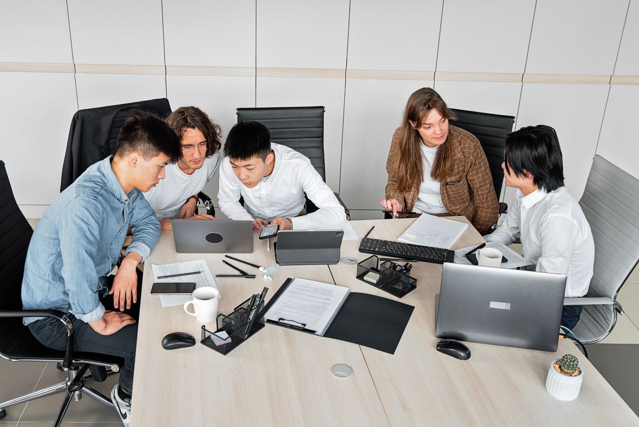 A diverse group of colleagues working together in an office setting with laptops and documents.